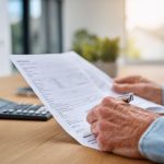 Mains avec des papiers d'évaluation immobilière et une calculatrice, illustrant la planification économique.